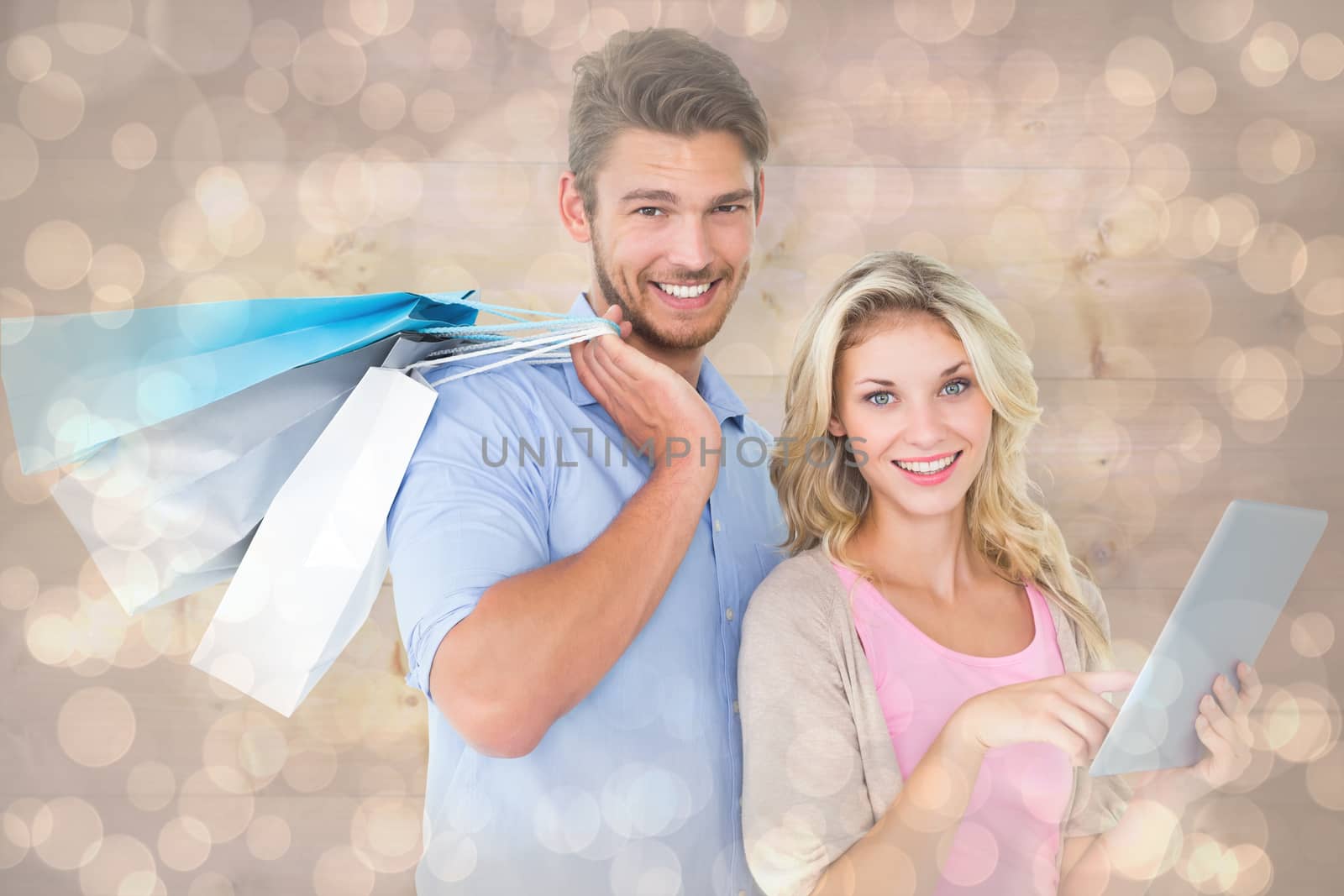 Attractive young couple holding shopping bags using tablet pc against light glowing dots design pattern