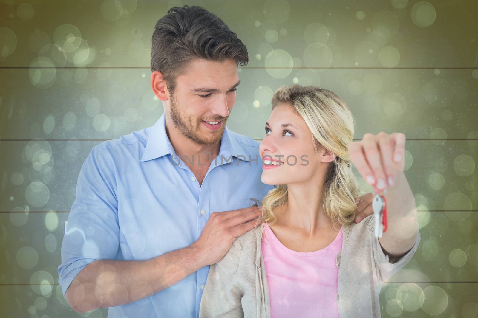 Attractive young couple showing new house key against blue abstract light spot design