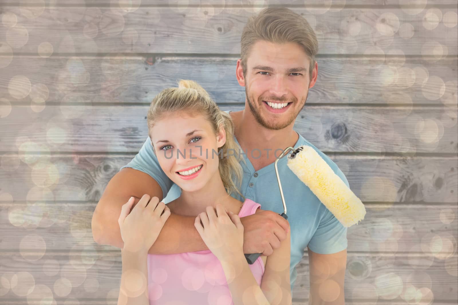 Young couple hugging and holding paint roller against light glowing dots design pattern