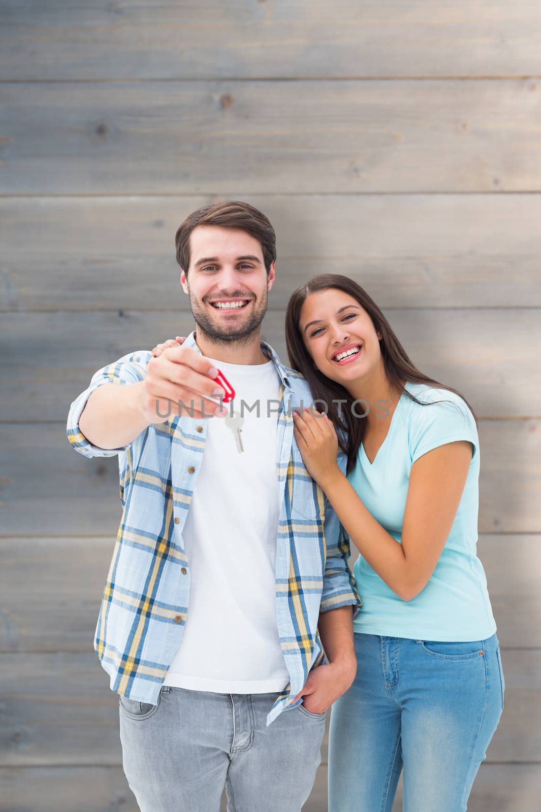 Happy young couple showing new house key against pale grey wooden planks
