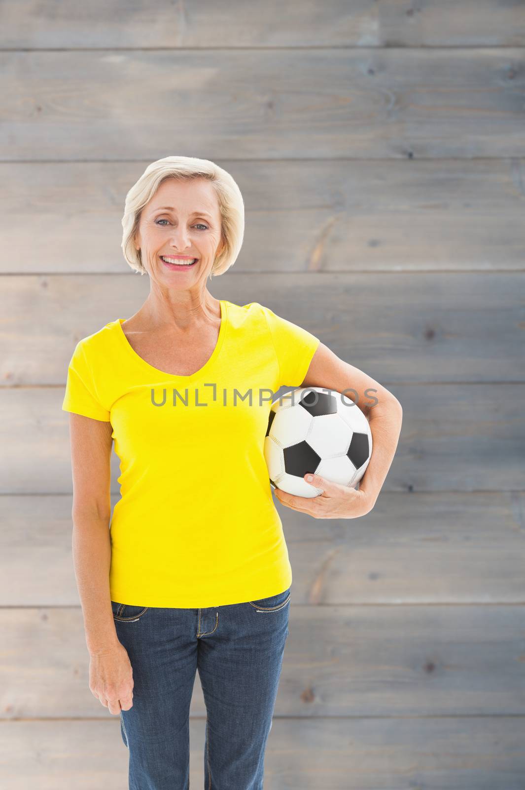 Composite image of mature blonde holding football smiling at camera by Wavebreakmedia