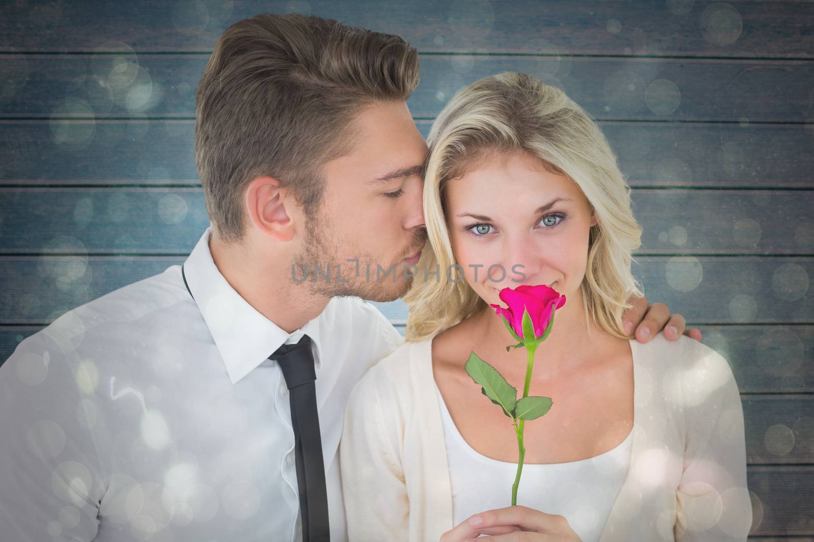 Handsome man kissing girlfriend on cheek holding a rose against black abstract light spot design