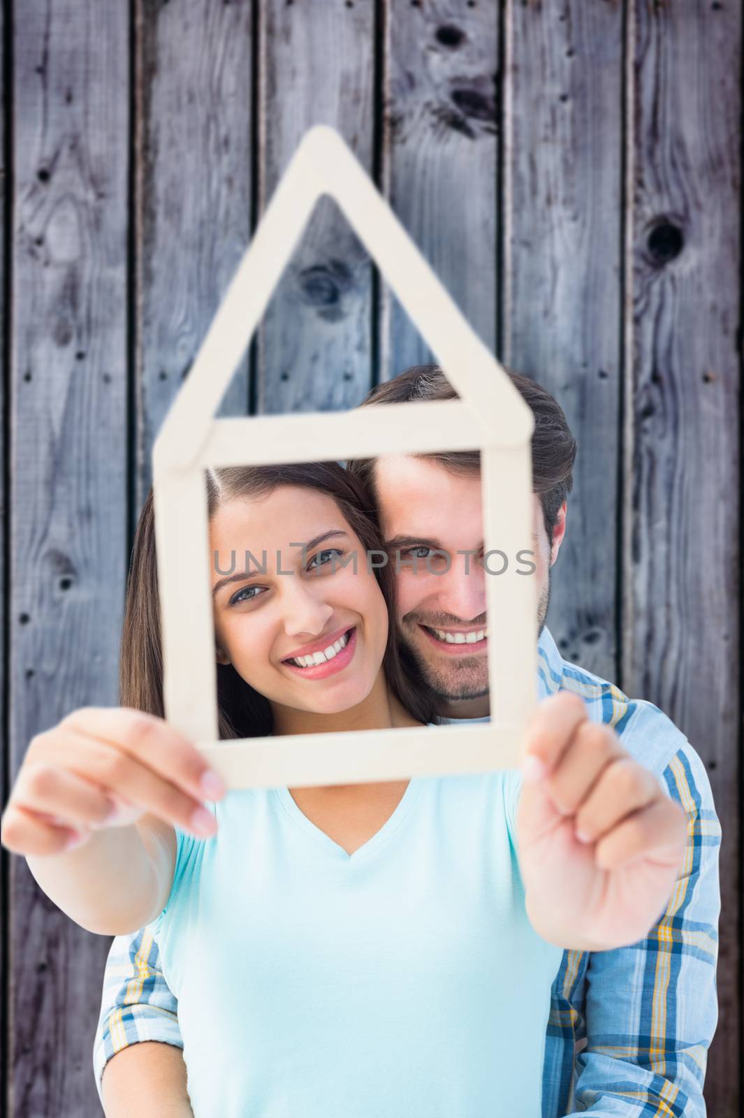 Happy young couple with house shape against grey wooden planks
