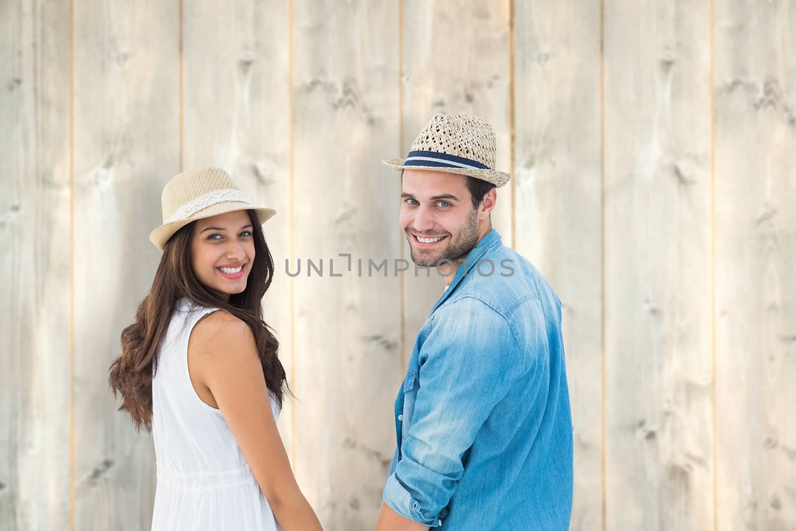 Happy hipster couple holding hands and smiling at camera against pale wooden planks