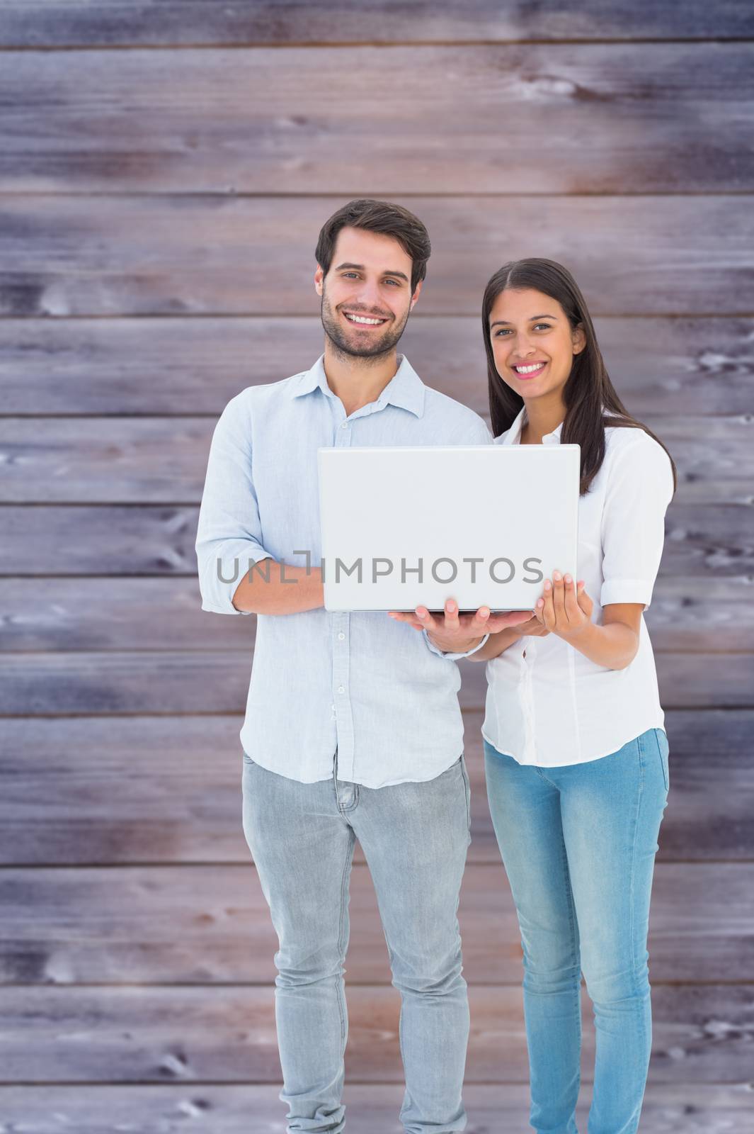 Attractive young couple holding their laptop against faded grey wooden planks