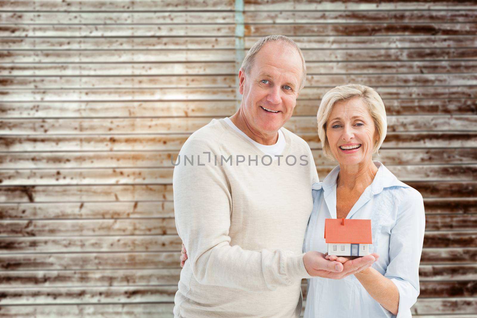Happy mature couple with model house against wooden planks