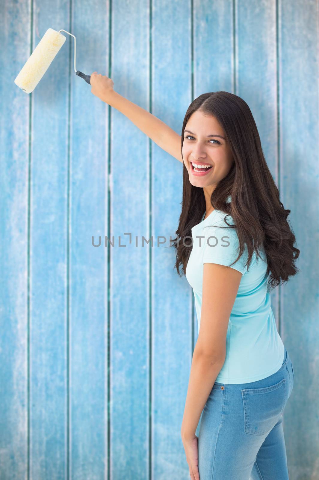 Composite image of happy young brunette painting with roller by Wavebreakmedia