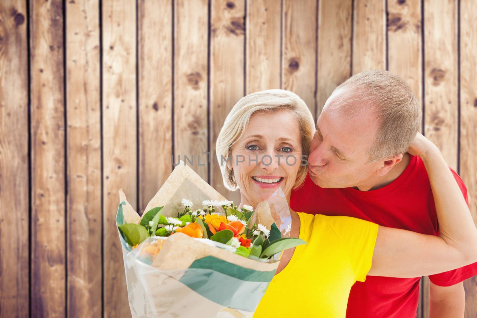 Mature man kissing his partner holding flowers against wooden planks