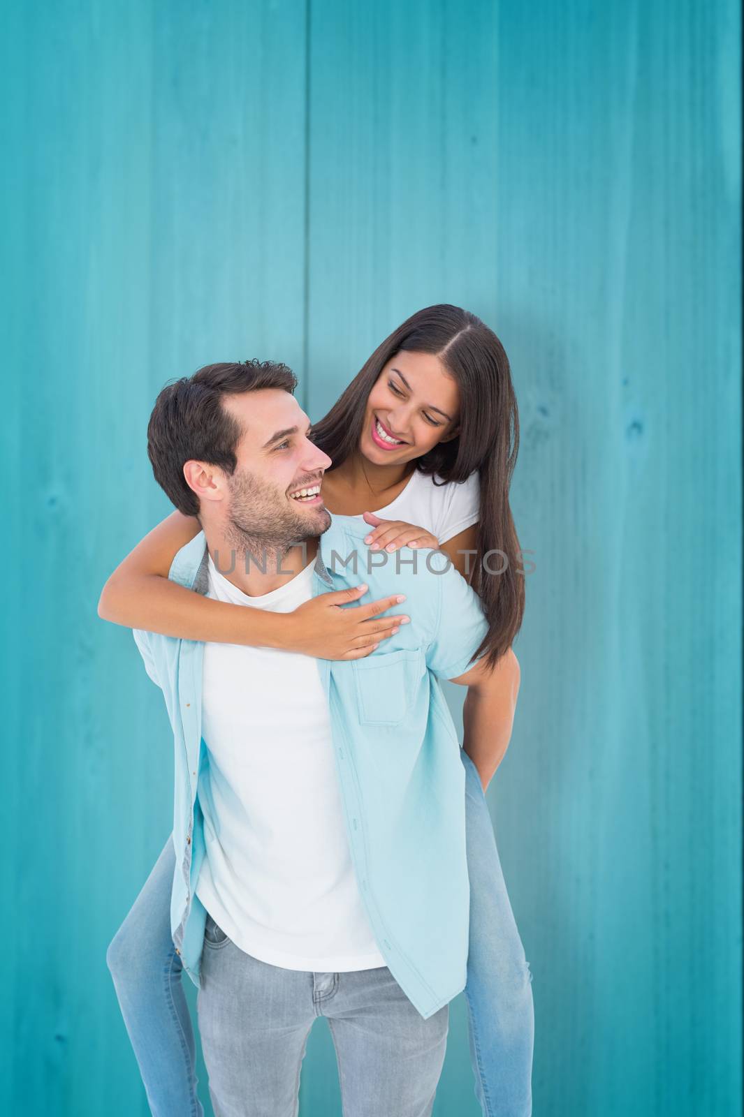 Happy casual man giving pretty girlfriend piggy back against wooden planks background