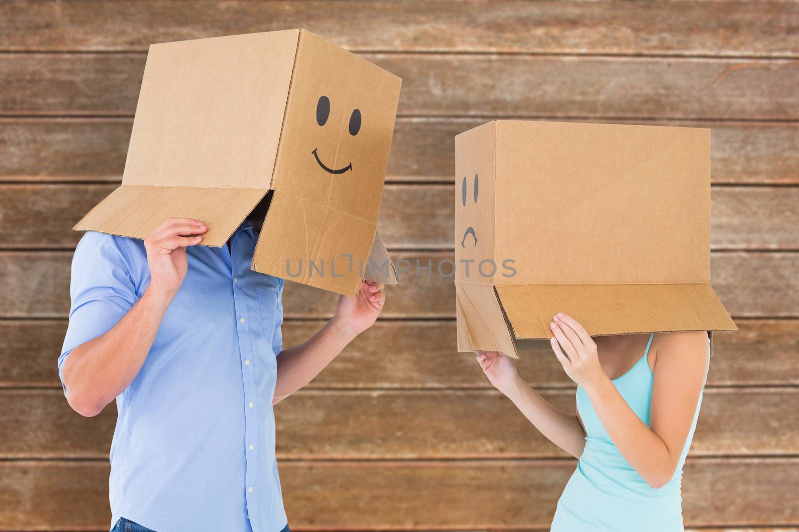 Couple wearing emoticon face boxes on their heads against wooden planks background
