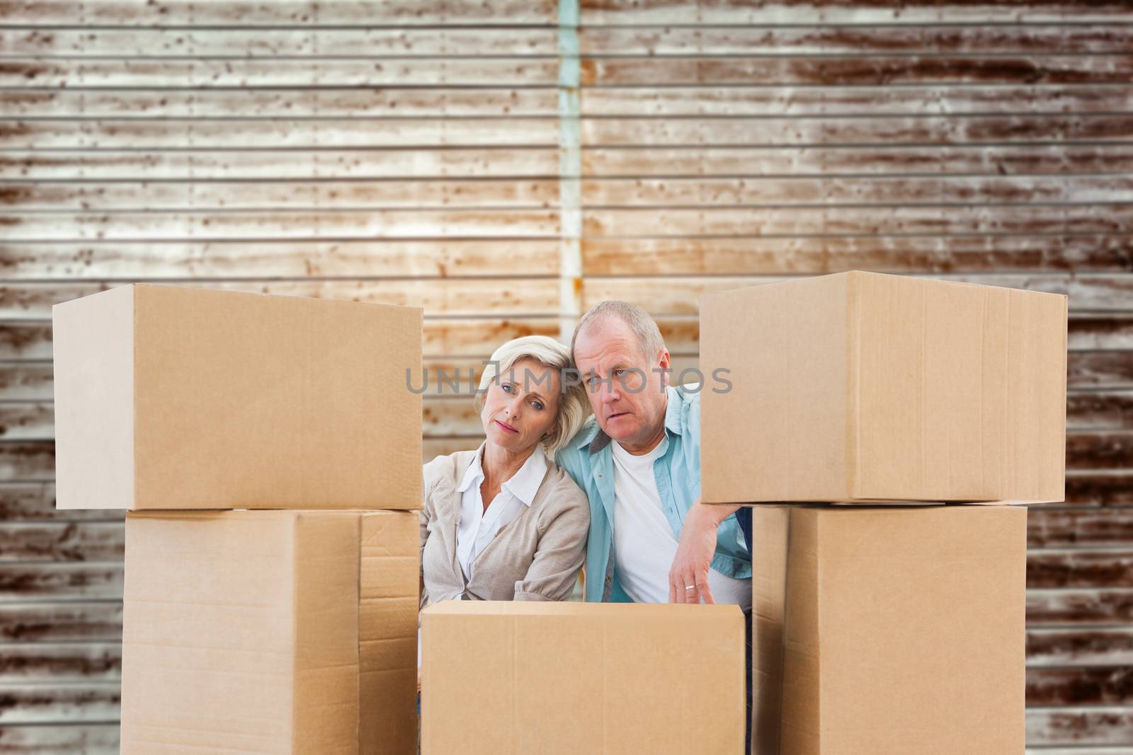 Stressed older couple with moving boxes against wooden planks