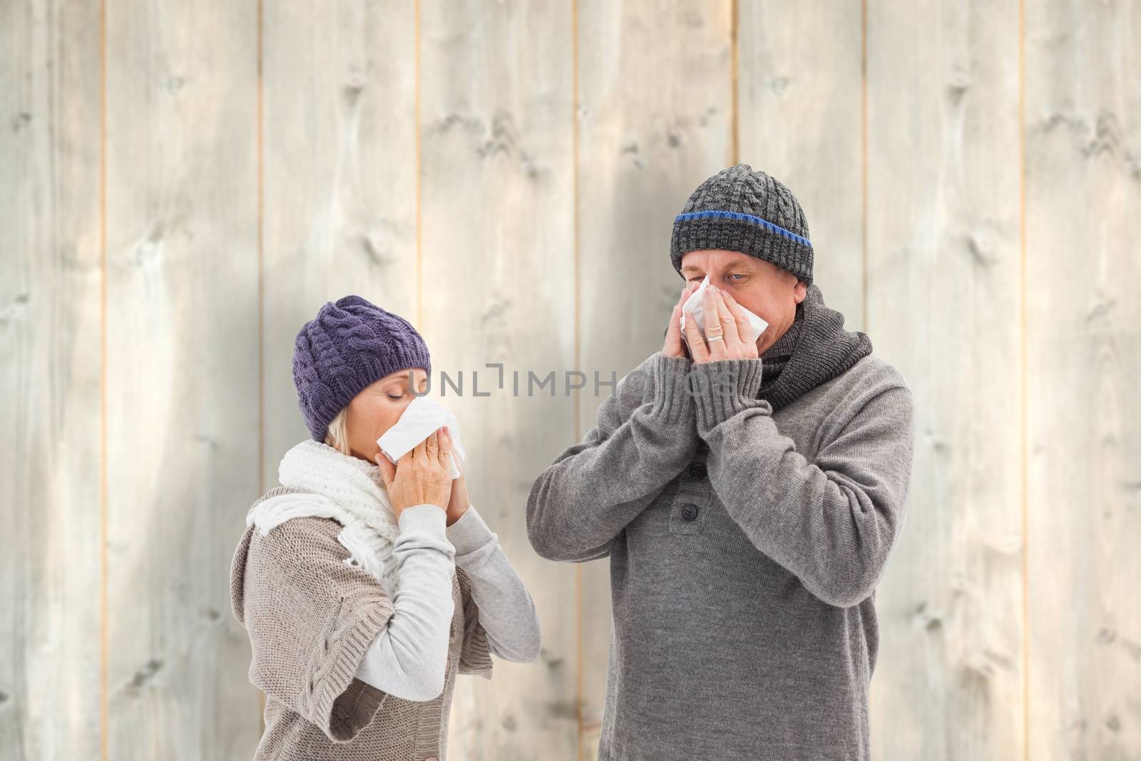 Sick mature couple blowing their noses against pale wooden planks