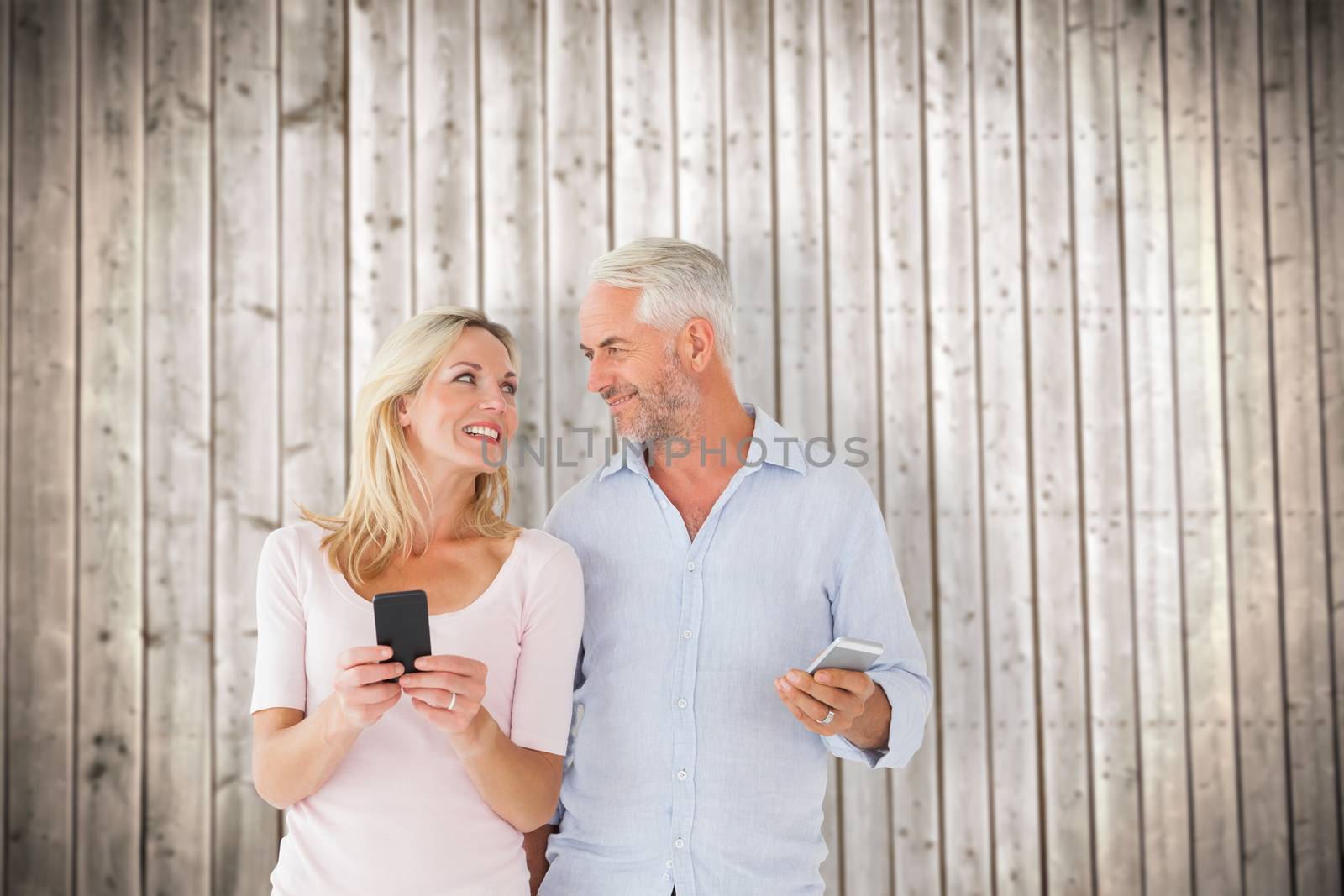 Happy couple texting on their smartphones against wooden planks background
