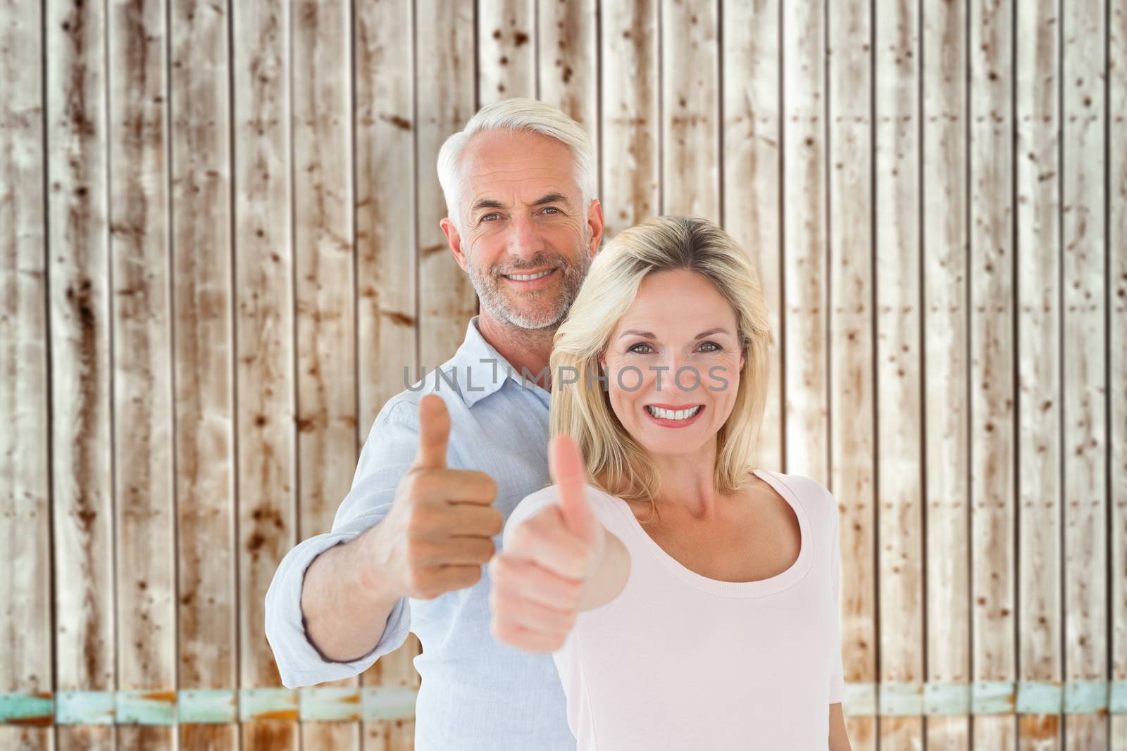 Smiling couple showing thumbs up together against faded pine wooden planks