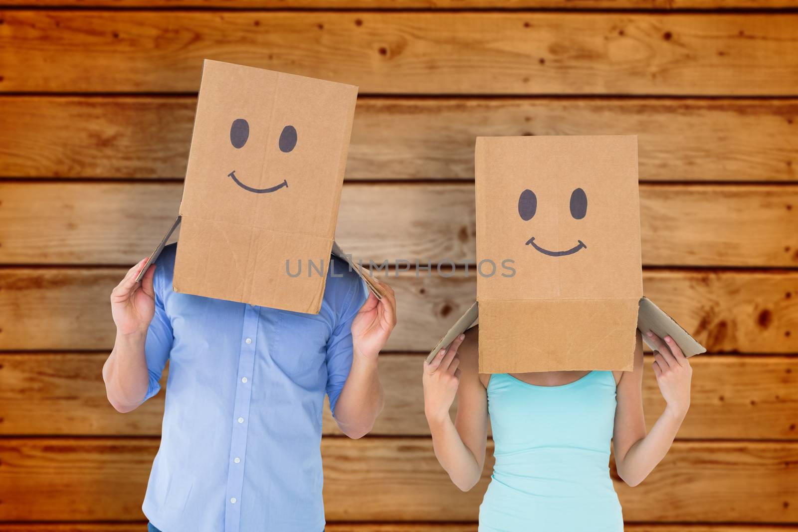 Couple wearing emoticon face boxes on their heads against wooden planks background