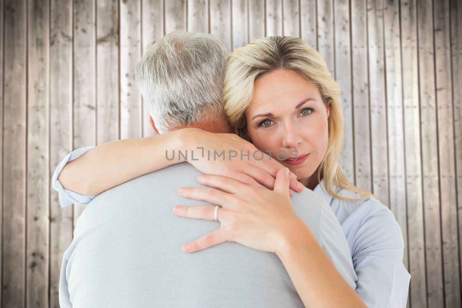 Unhappy blonde hugging her husband against wooden planks background