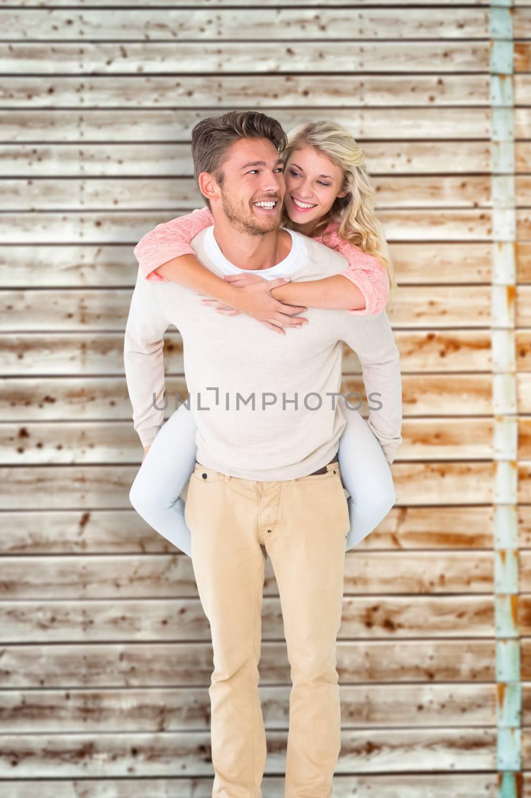 Handsome man giving piggy back to his girlfriend against faded pine wooden planks