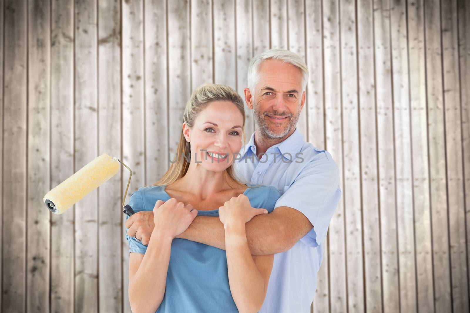 Happy couple hugging and holding paint roller against wooden planks background