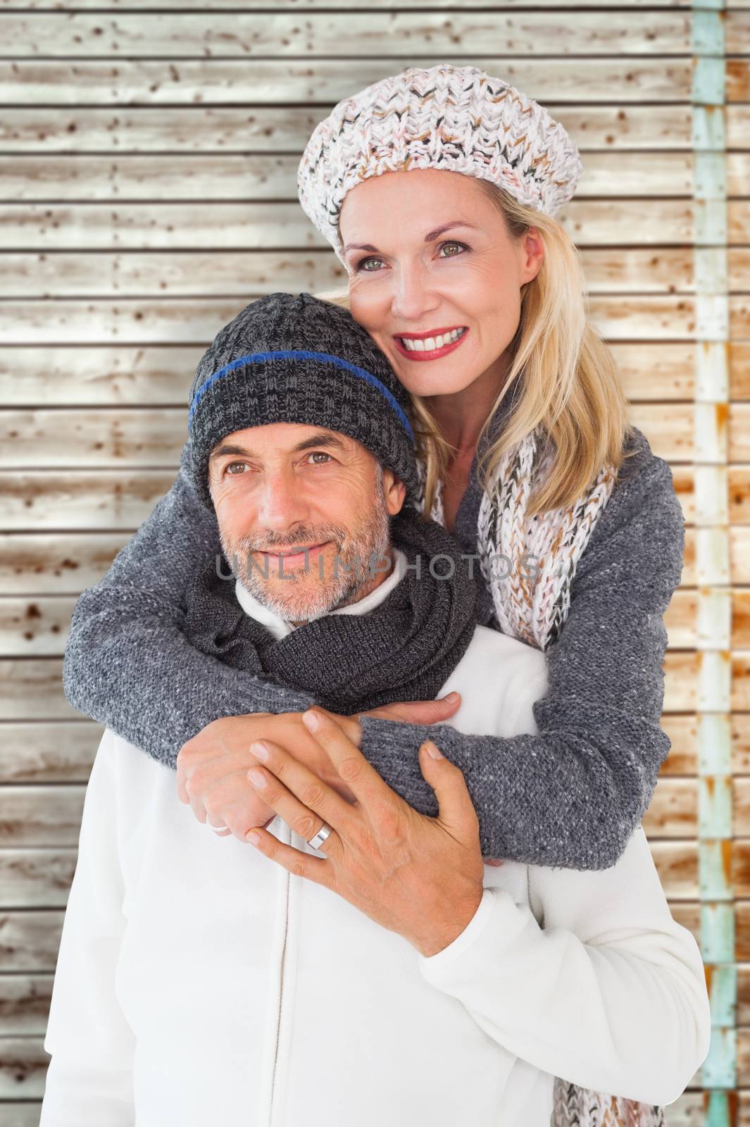 Happy couple in winter fashion embracing against faded pine wooden planks