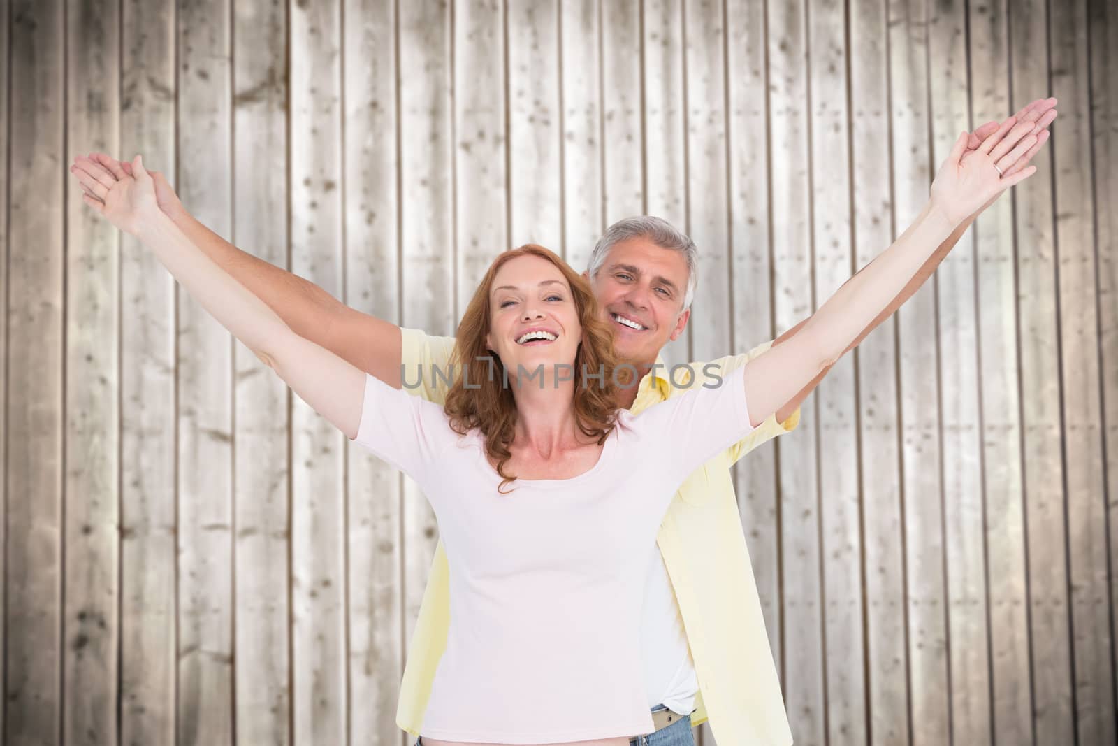 Casual couple smiling with arms raised against wooden planks background