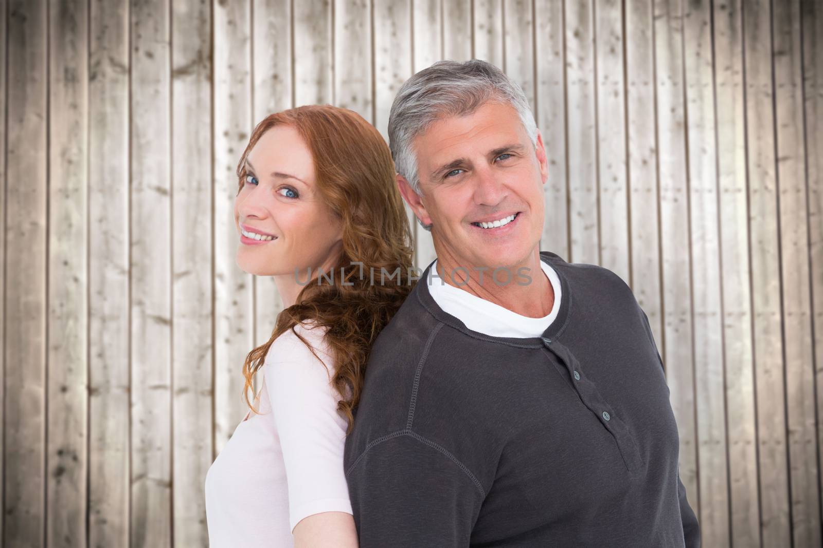 Casual couple smiling at camera against wooden planks background