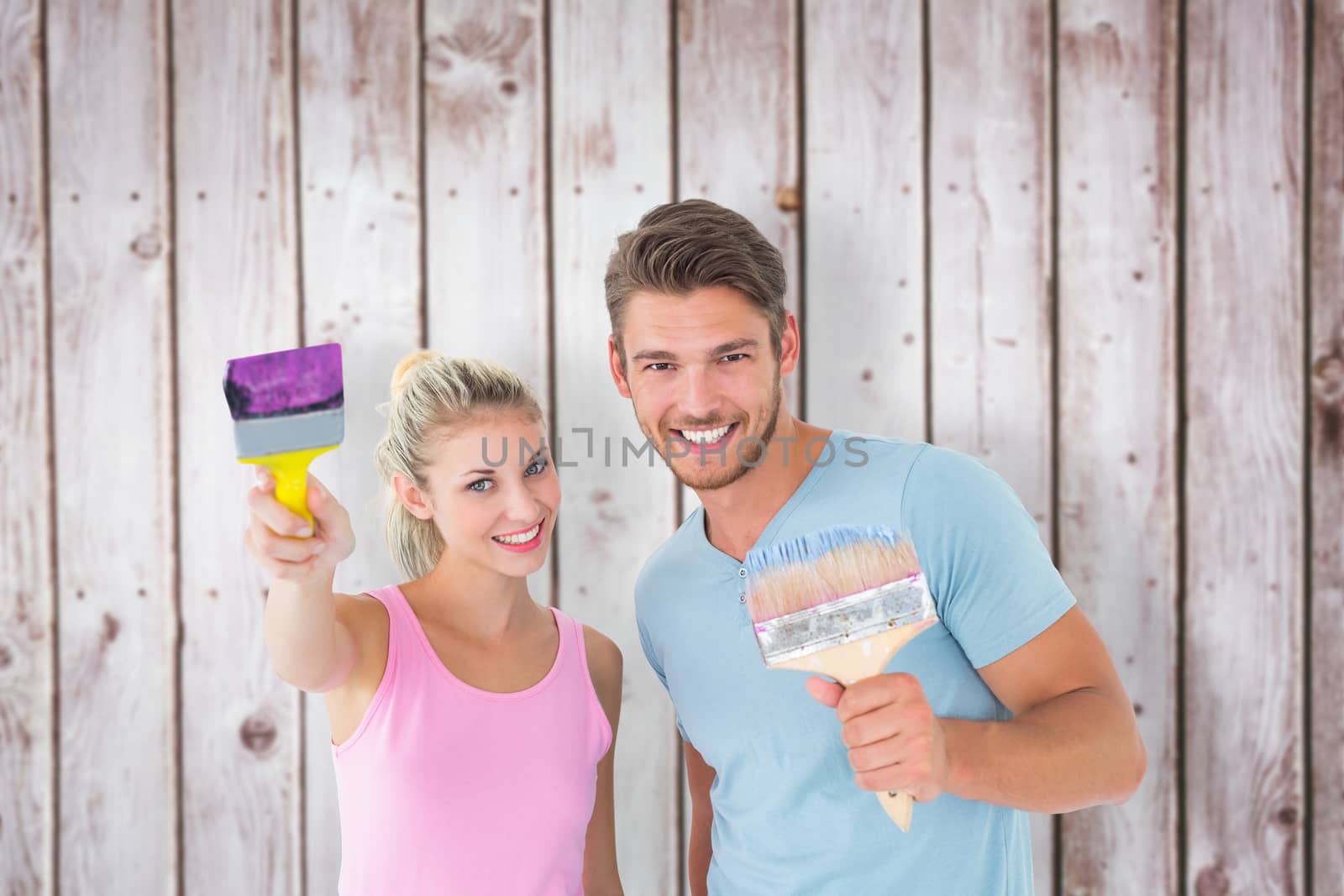 Composite image of young couple smiling and holding paintbrushes  by Wavebreakmedia