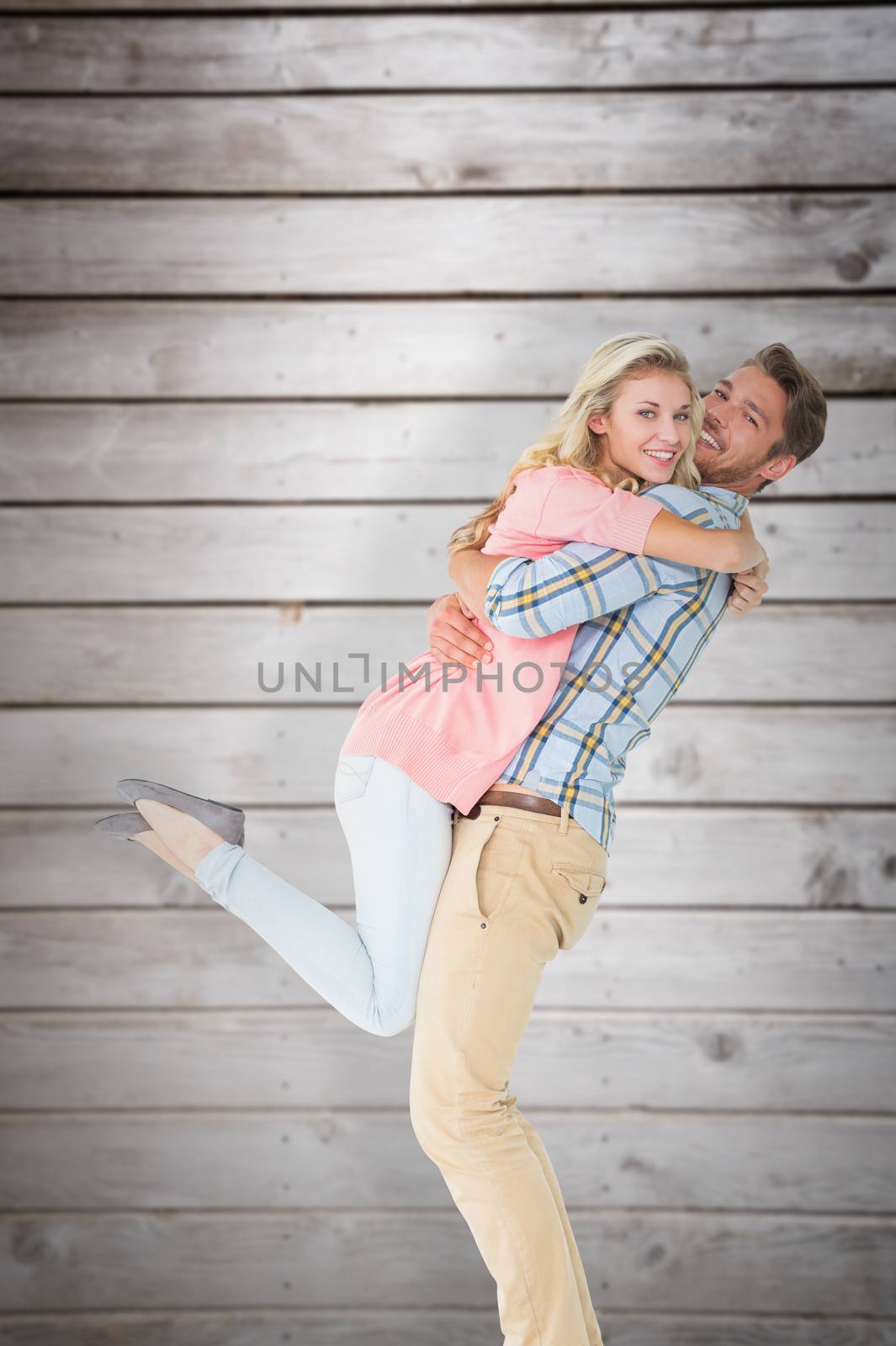 Handsome man picking up and hugging his girlfriend against wooden planks