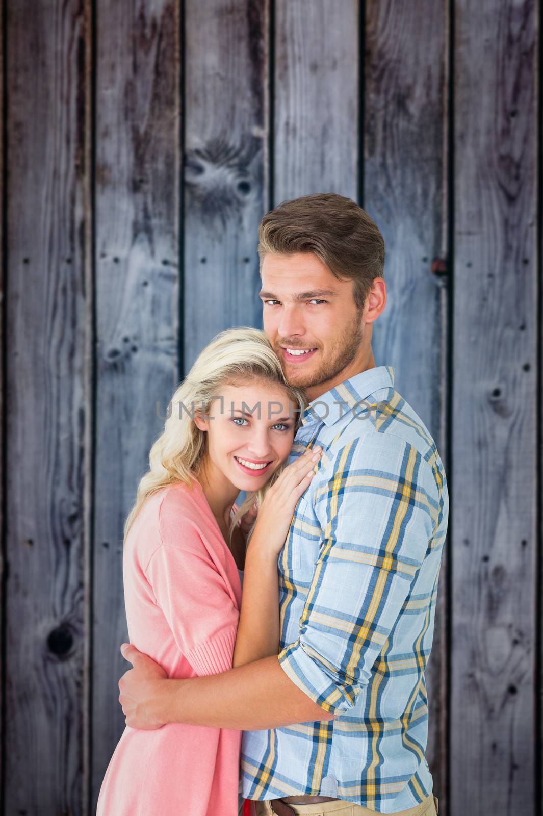 Attractive couple embracing and smiling at camera against grey wooden planks