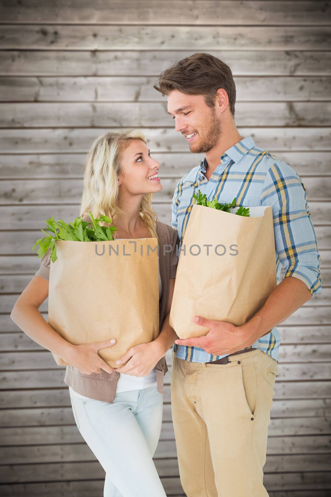 Attractive couple holding their grocery bags against wooden planks background