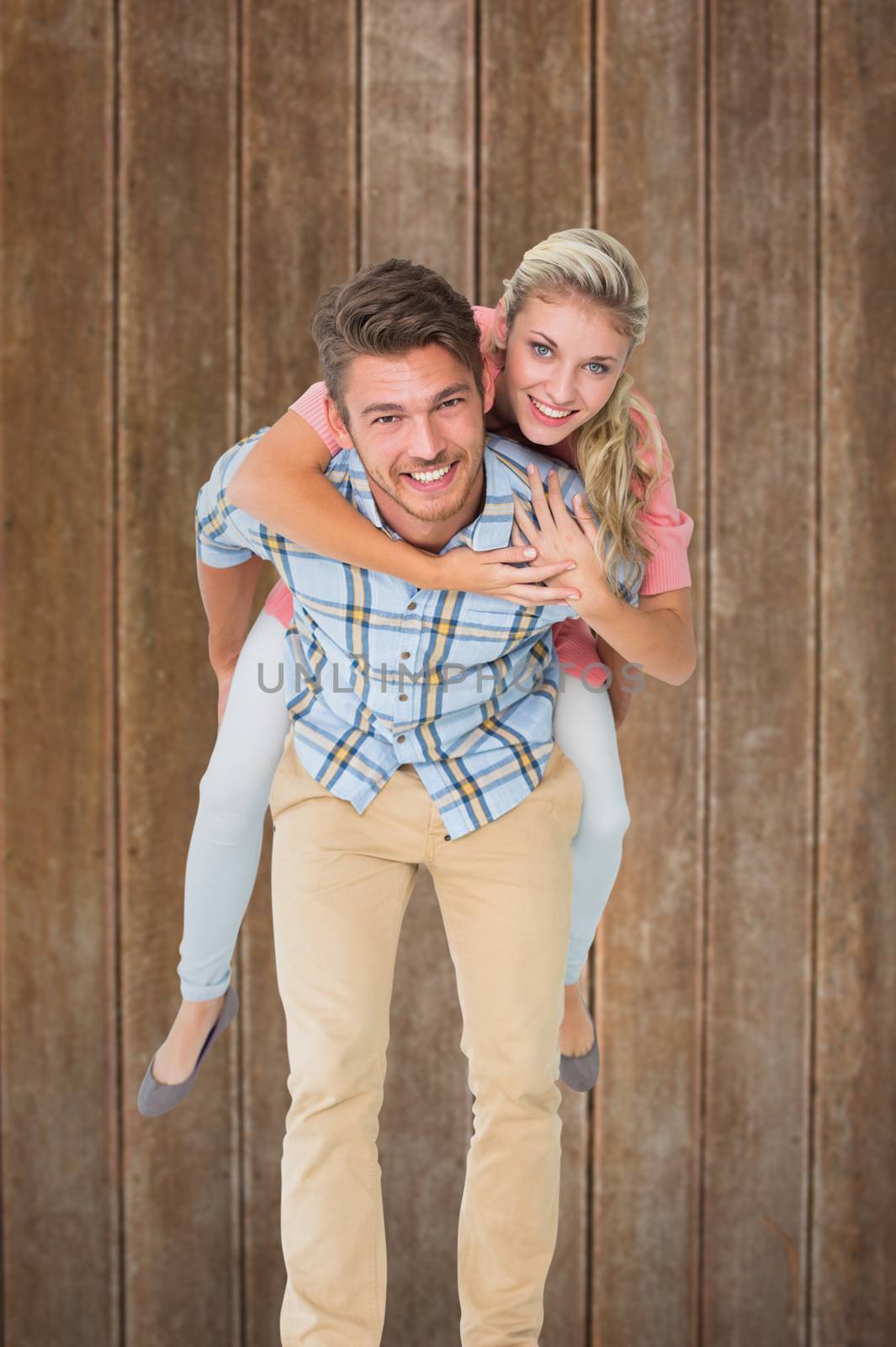 Handsome man giving piggy back to his girlfriend against wooden planks background