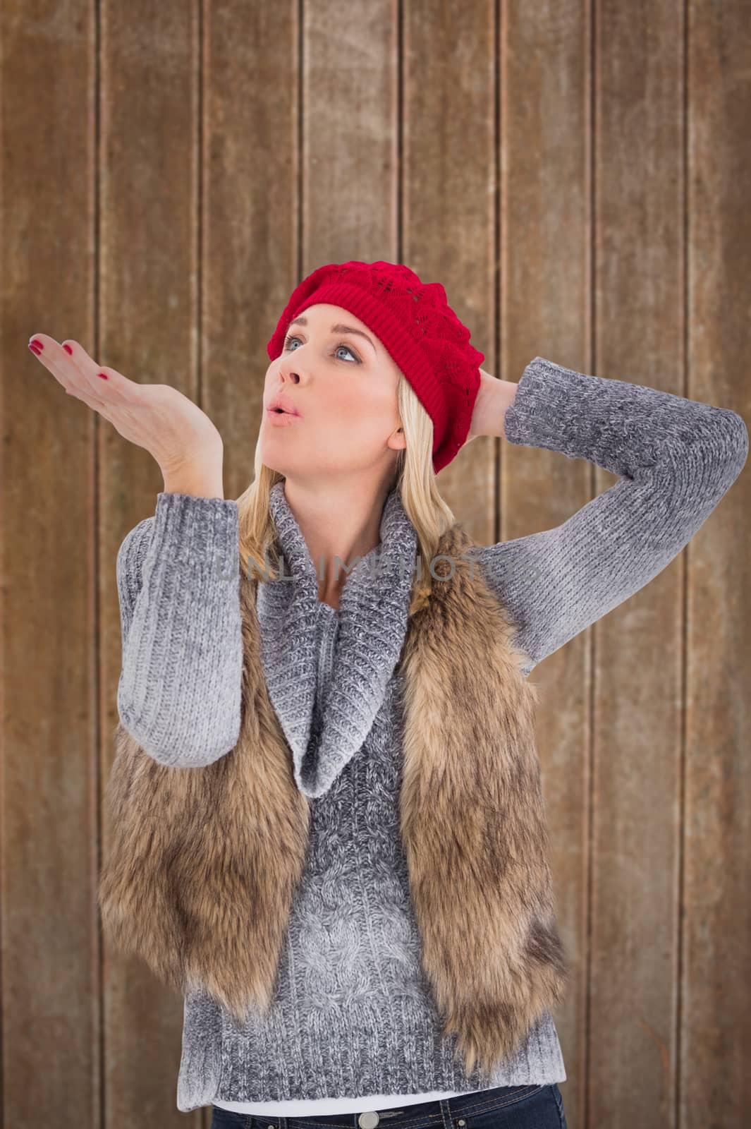 Blonde in winter clothes blowing kiss against wooden planks background