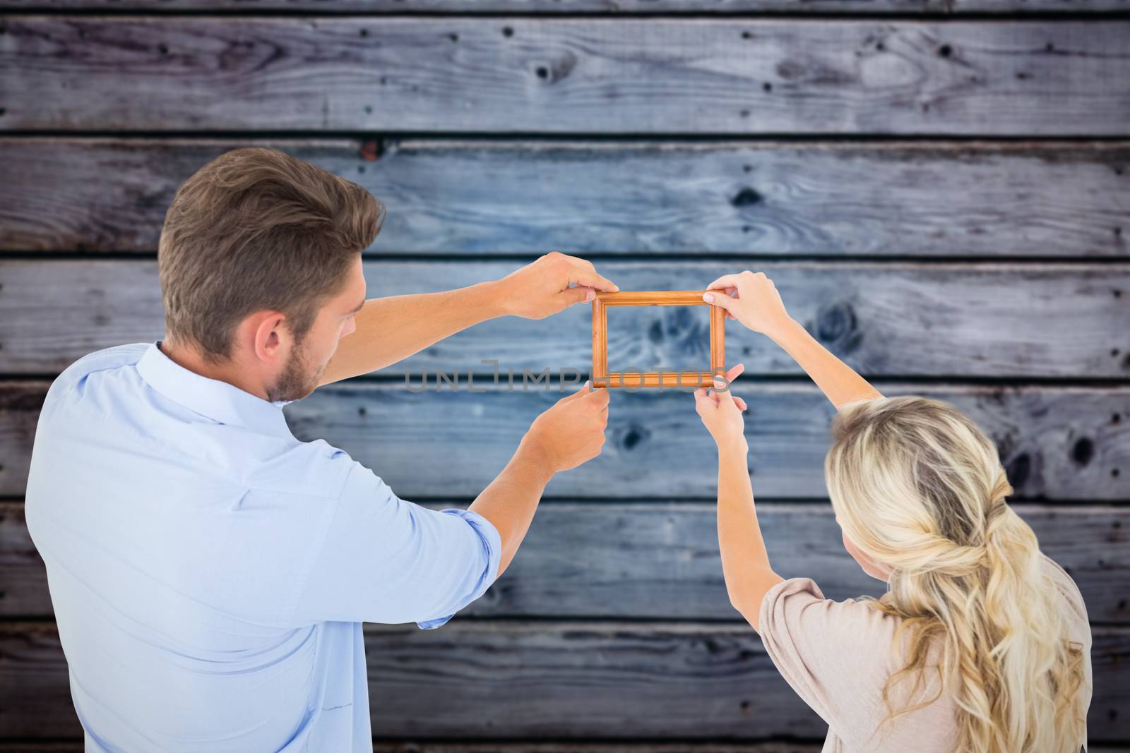 Attractive young couple hanging a frame against grey wooden planks