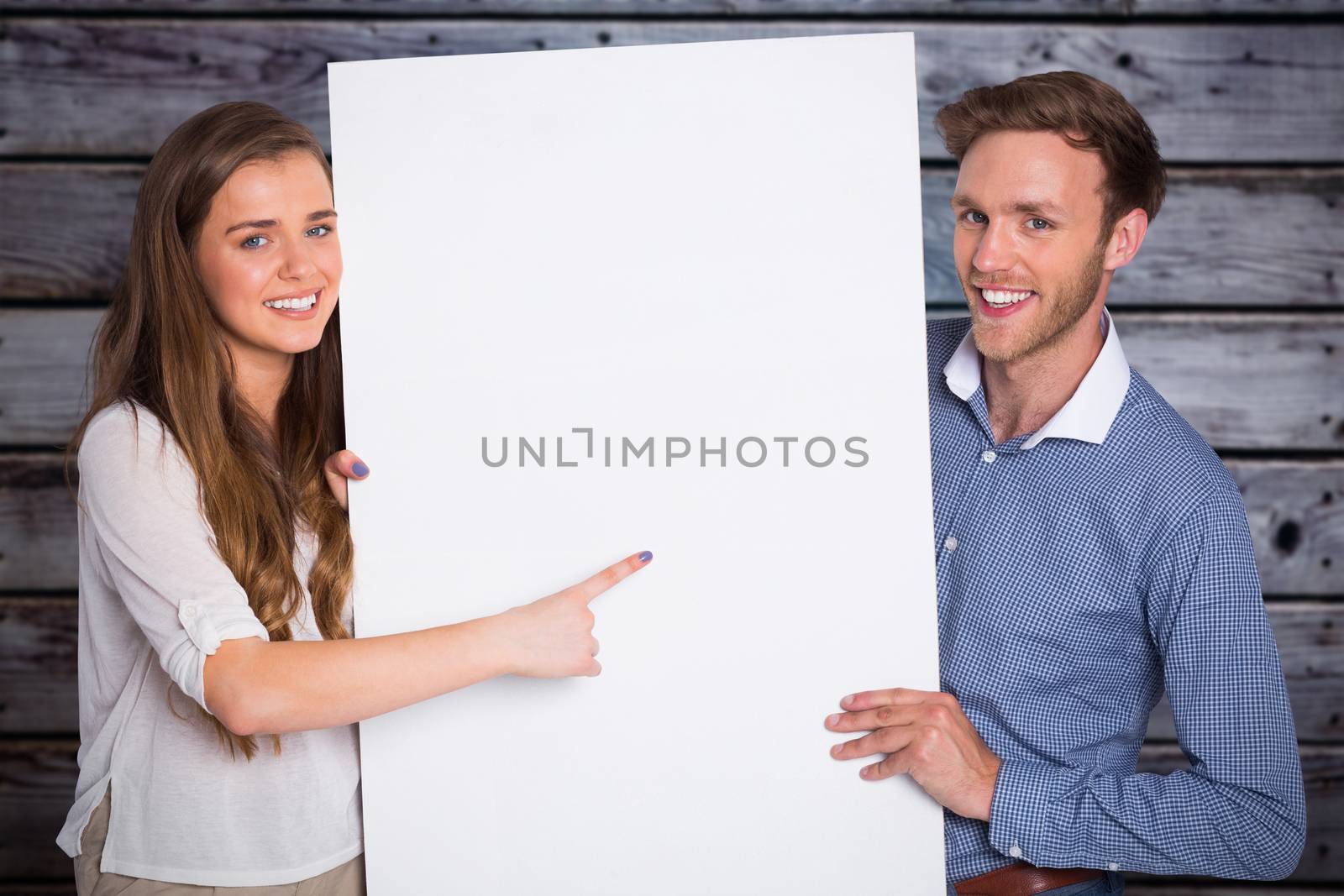 Happy young couple with blank board against grey wooden planks