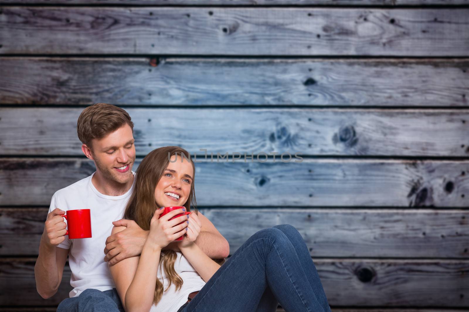 Composite image of couple with coffee cups sitting on floor by Wavebreakmedia