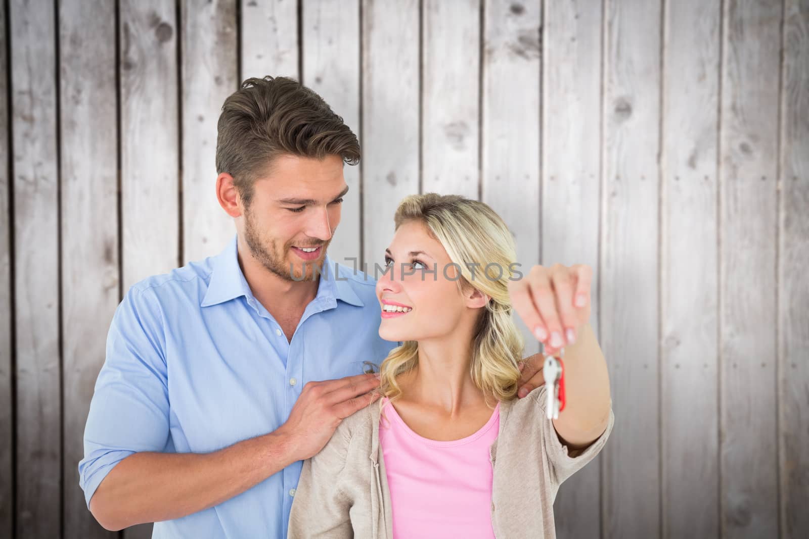 Attractive young couple showing new house key against wooden planks