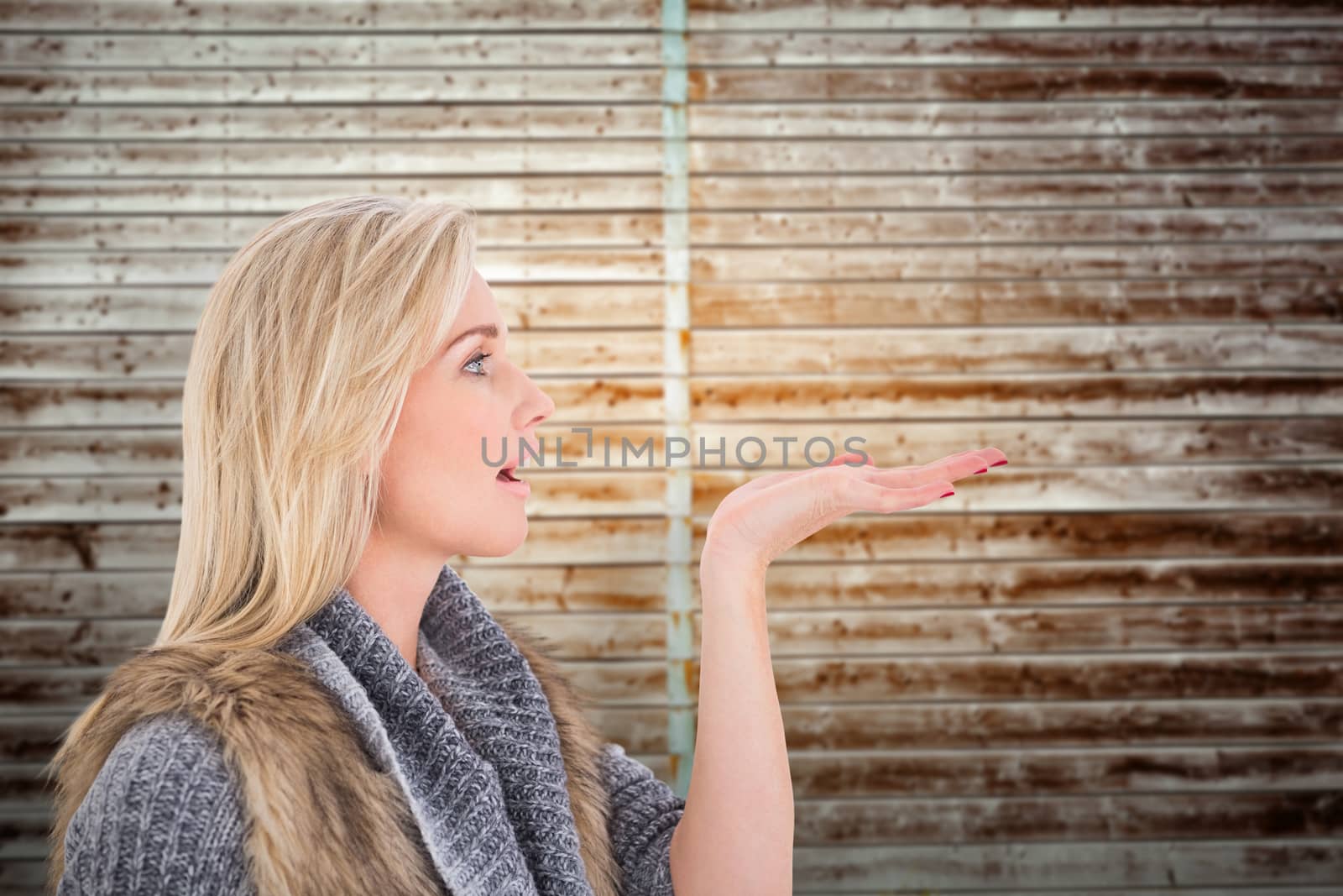 Blonde in winter clothes with hand out against wooden planks