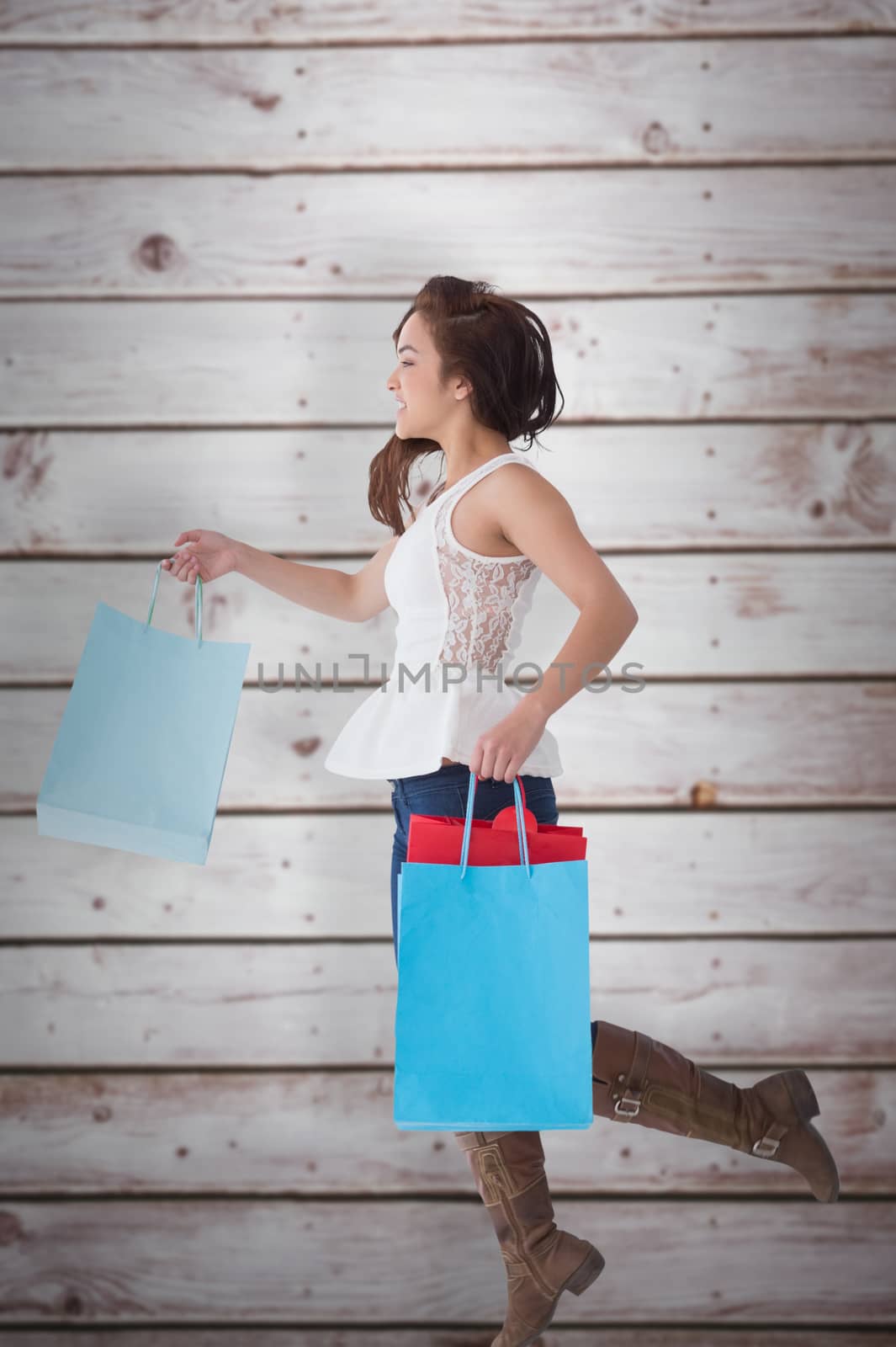 Happy brunette leaping with shopping bags against wooden planks