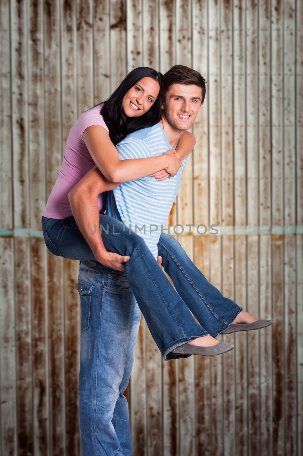 Young man giving girlfriend a piggyback ride against wooden planks