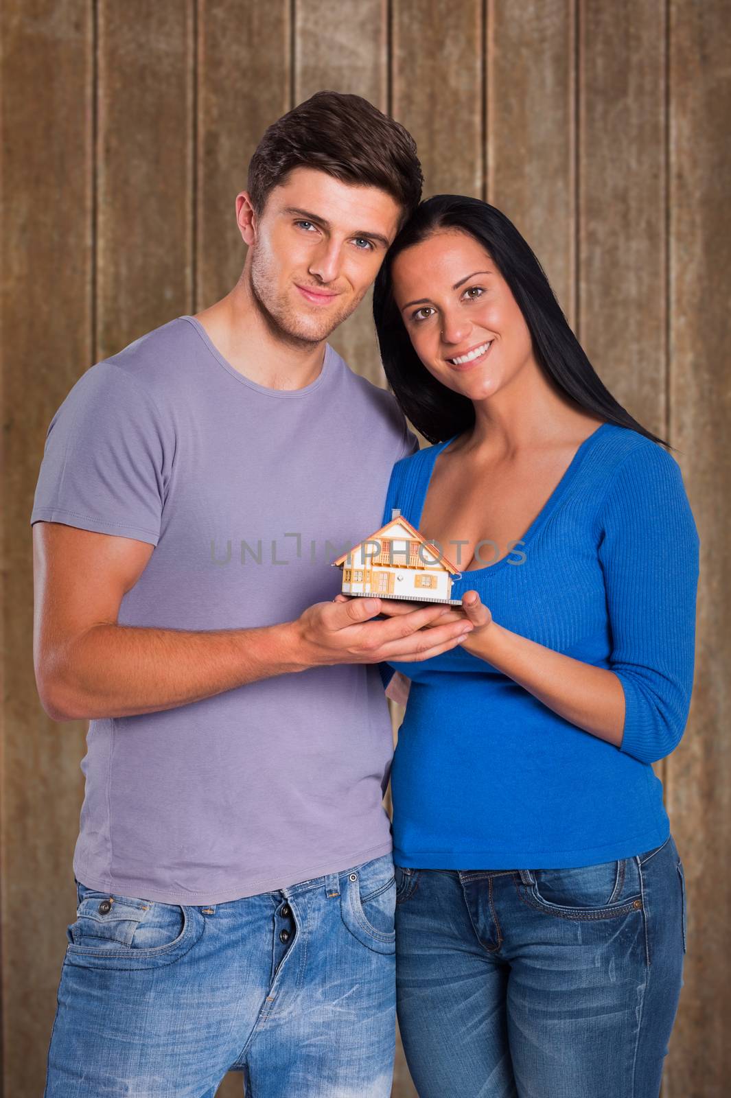 Young couple holding a model house against wooden planks background