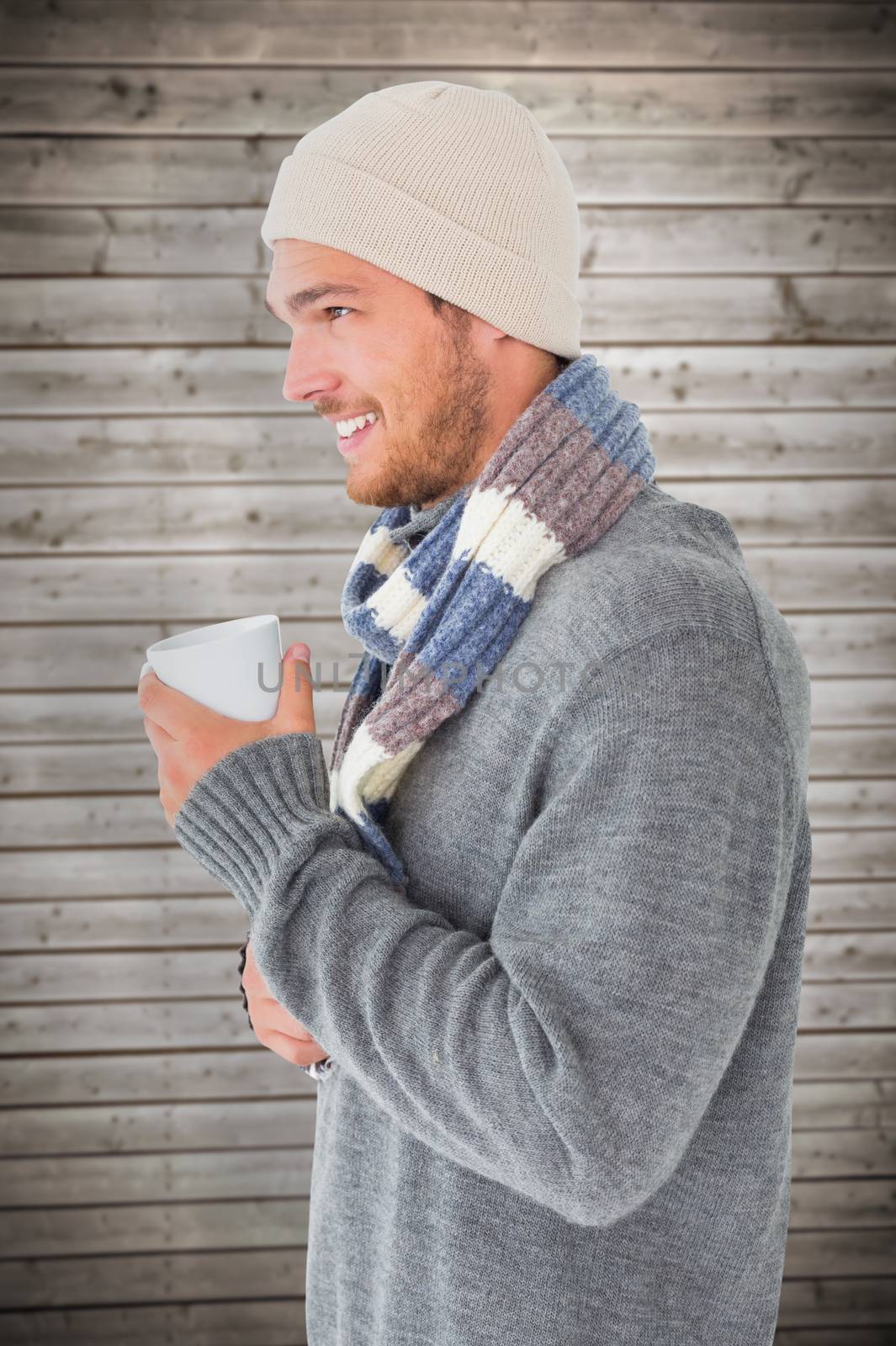 Handsome man in winter fashion holding mug against wooden planks background