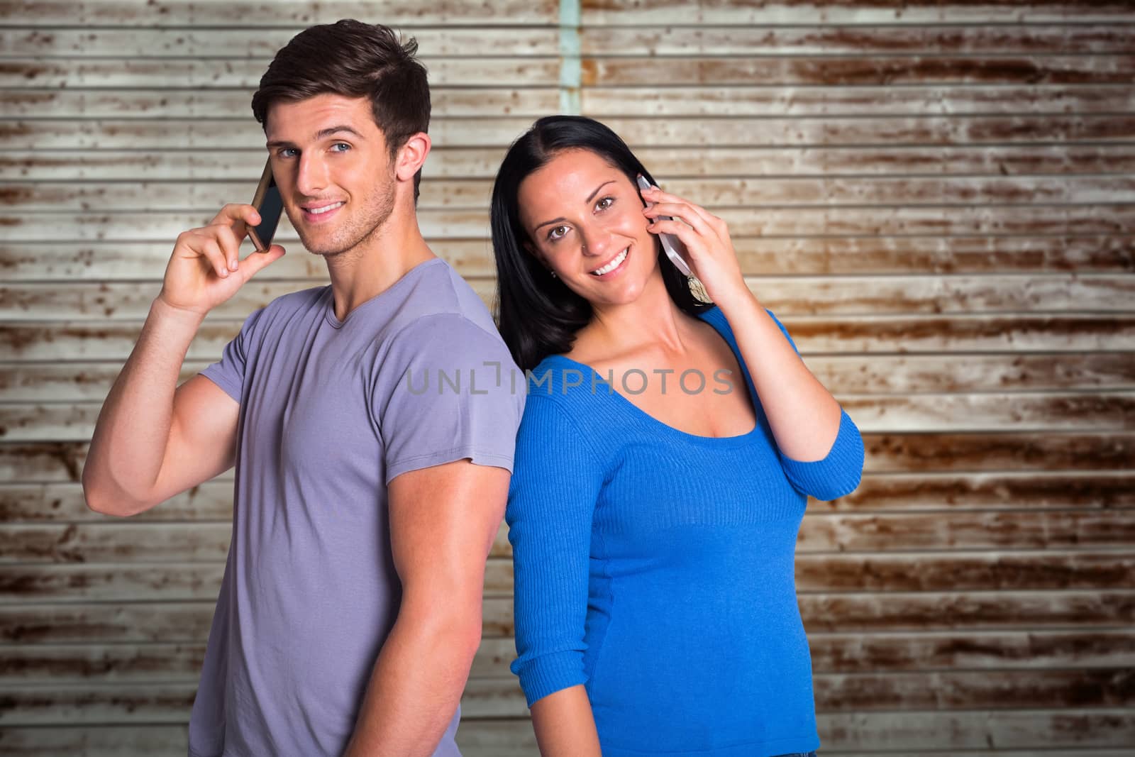 Young couple talking on their phones against wooden planks