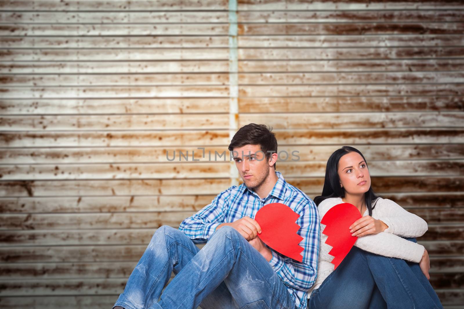 Young couple sitting on floor with broken heart against wooden planks