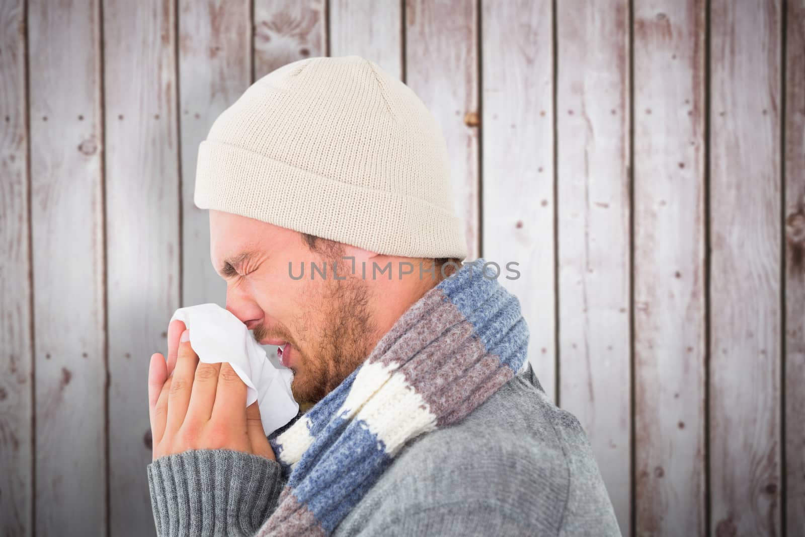 Handsome man in winter fashion blowing his nose against wooden planks