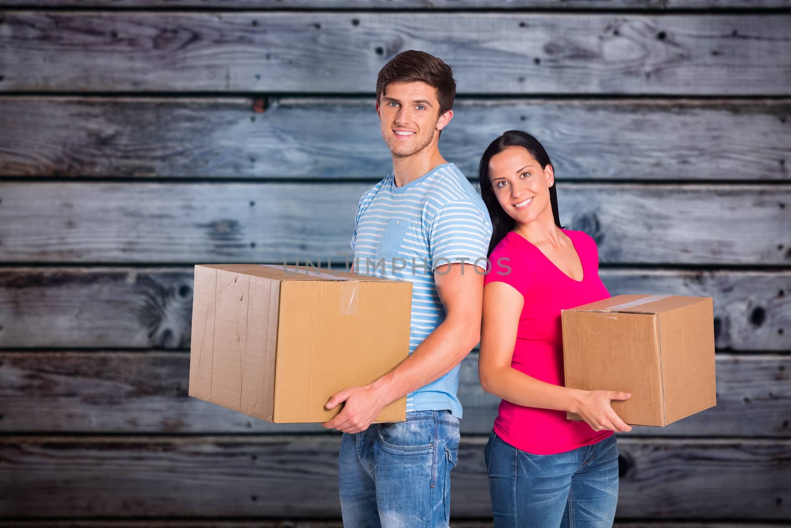 Young couple holding moving boxes against grey wooden planks