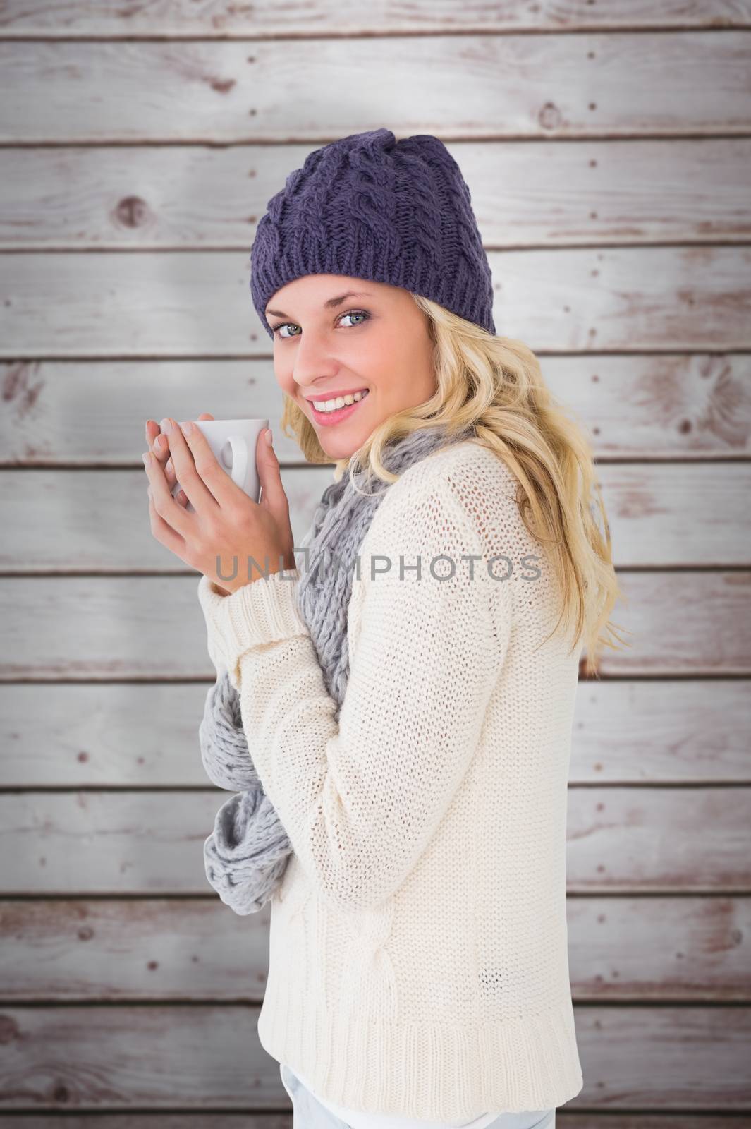 Pretty blonde in winter fashion holding mug against wooden planks