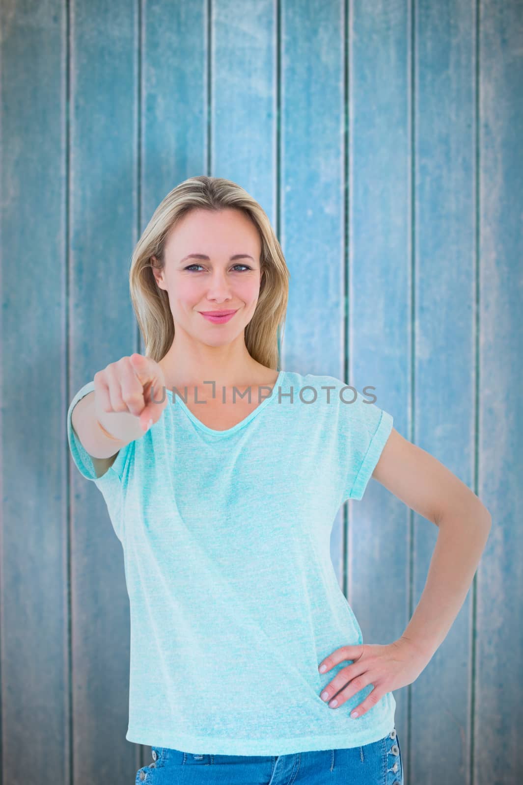 Smiling blonde standing and pointing at camera against wooden planks