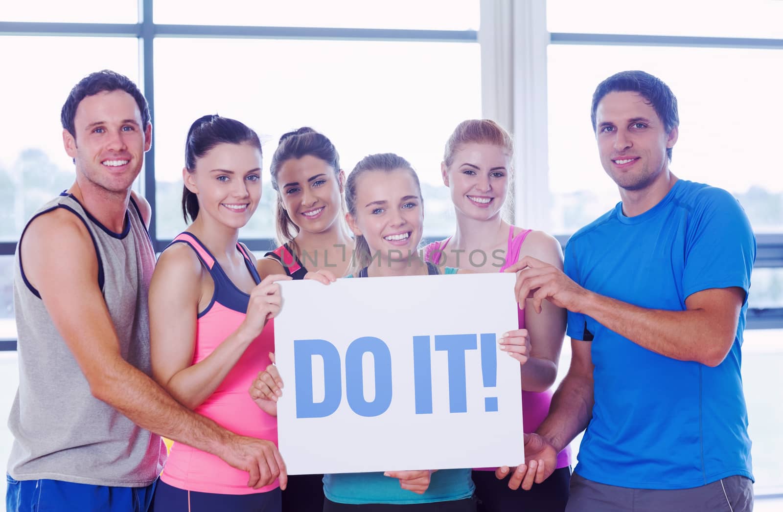 The word do it! against portrait of a group of fitness class holding blank paper