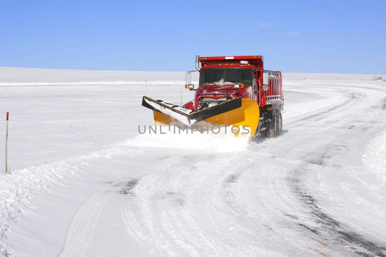 A snowplow truck removing snow from a winding rural road on bright winter day.