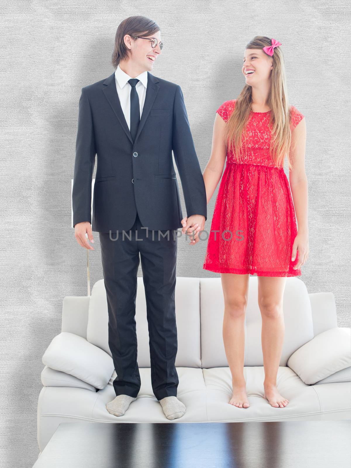 Geeky couple standing hand in hand on the couch against white background