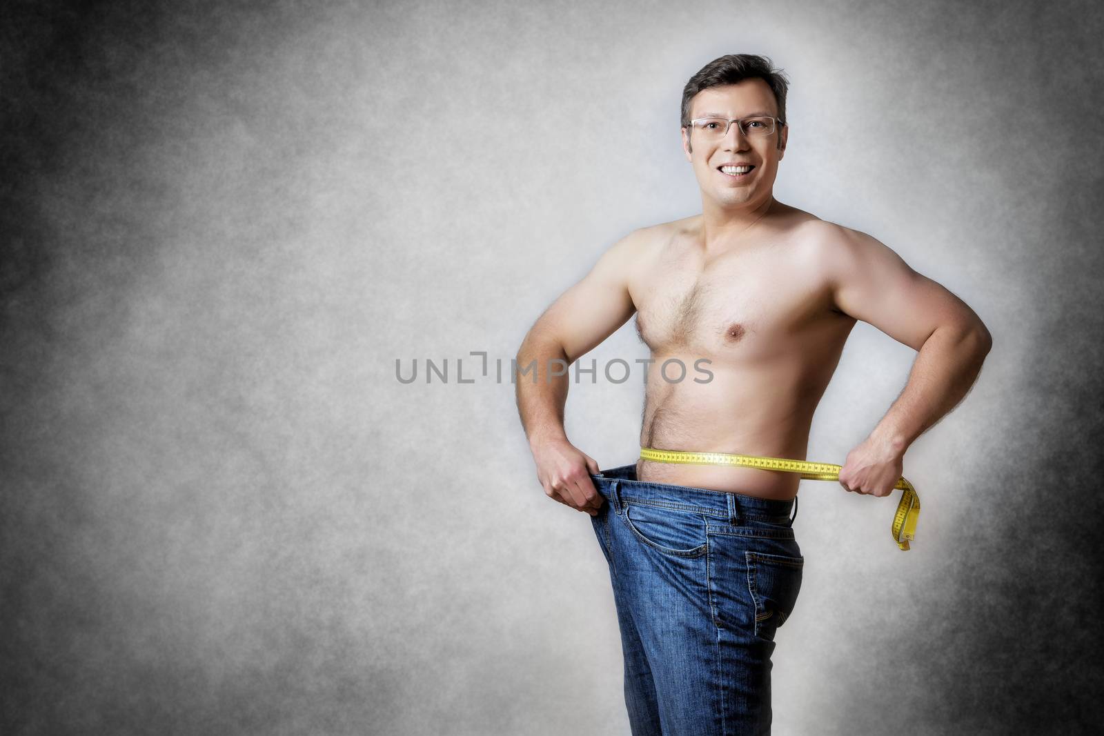 Image of a man in blue jeans with measuring tape who has lost body weight